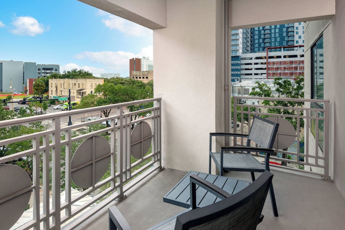 Un balcon avec une table et des chaises, une vue sur le paysage urbain et un immeuble doté d’un parking.
