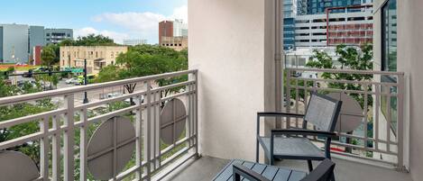 A balcony with a table and chairs, a view of a cityscape, and a building with a parking garage.