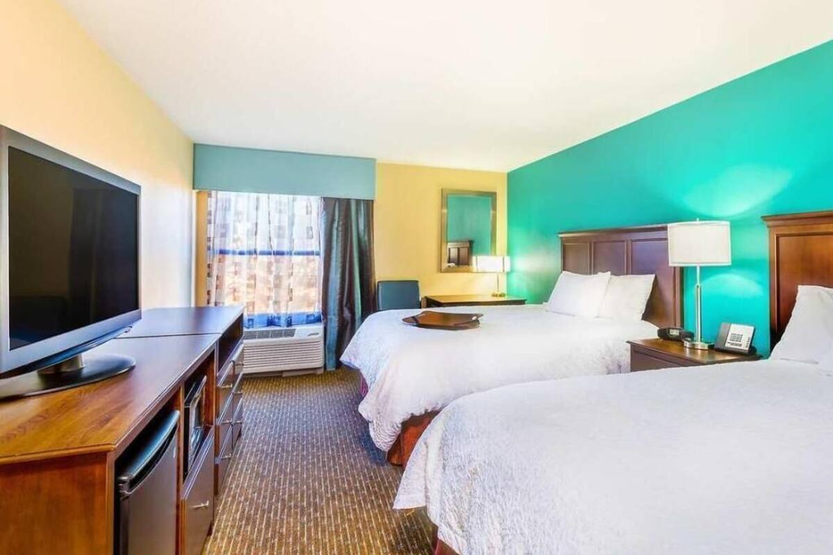 A hotel room with a television, two beds, a desk, and a window with curtains.
