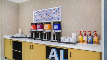 Estação de café com quatro dosadores identificados como 'Quente', 'Suave', 'Descafeinado' e 'Torra Escura'. Também há quatro garrafas de leite para café.