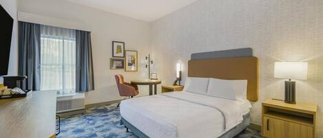 Een hotelkamer met een groot bed, een bureau met stoel, een bijzettafeltje en een nachtkastje met lamp.