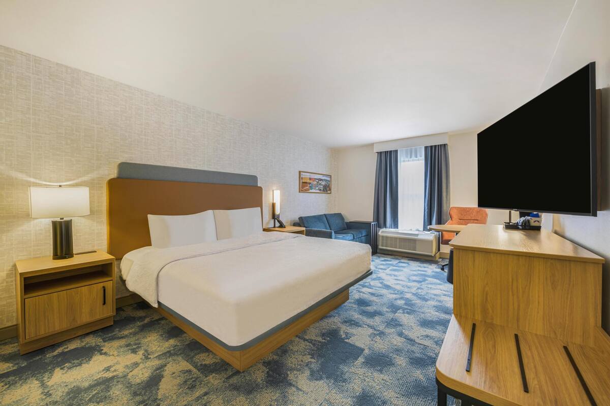 A hotel room with a bed, a desk, a television, a sofa, and a window with curtains.