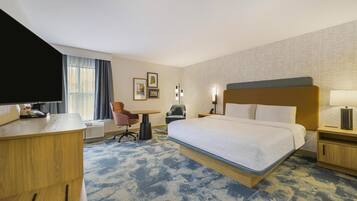 A hotel room with a large bed, a desk, a chair, a TV, and a window with curtains.