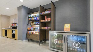 A self-service beverage station with refrigerated drink dispensers and a variety of snacks and beverages on shelves. - Hampton Inn Huntsville-Arsenal/South Pkway (Huntsville)