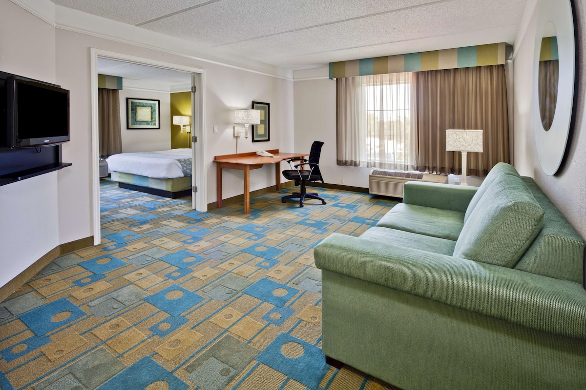 A hotel room with a bed, a desk, a green sofa, a TV, and a patterned carpet.