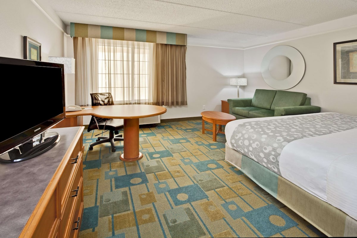 A hotel room with a bed, a desk with a computer, a TV, a green sofa, and a patterned carpet.