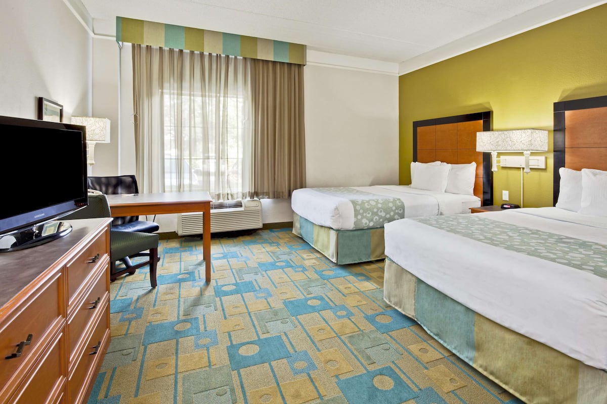 A hotel room with two beds, a desk, a television, and a window with curtains.