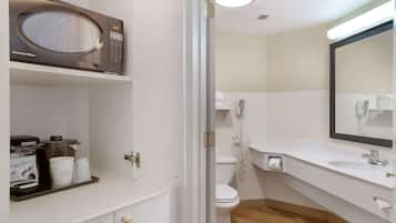 A hotel bathroom with a microwave, coffee maker, and toiletries on the counter.