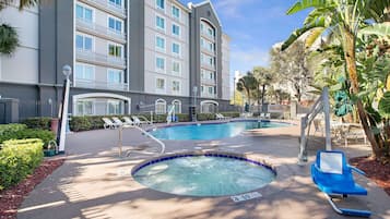Relax by the pool with a hot tub at the center, surrounded by lounge chairs and umbrellas.