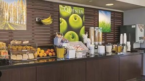 Una barra de desayuno con diversos alimentos y bebidas, un cartel grande con manzanas verdes y un refrigerador.