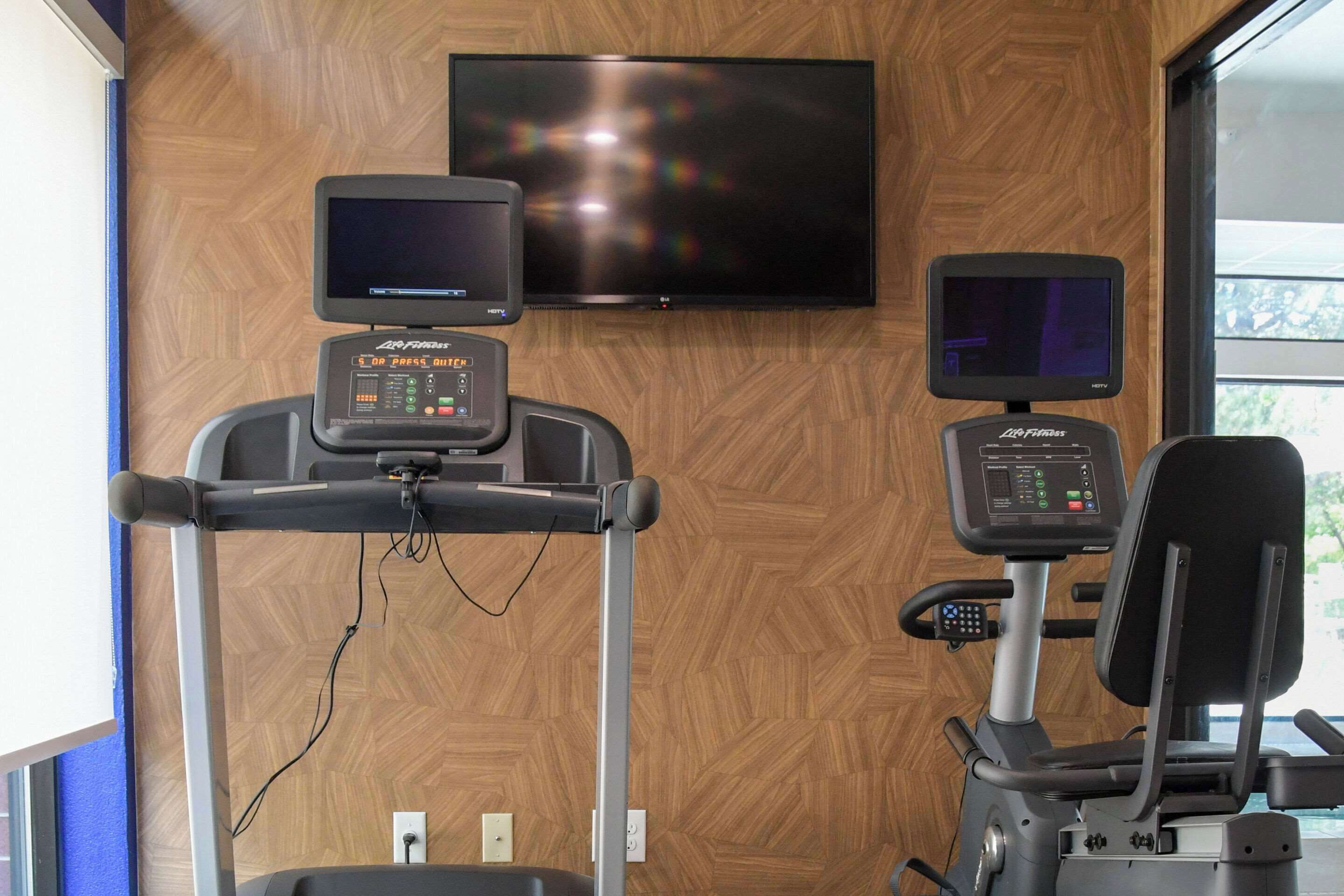 Un gimnasio con cintas de correr, una bicicleta estática y un televisor montado en la pared.