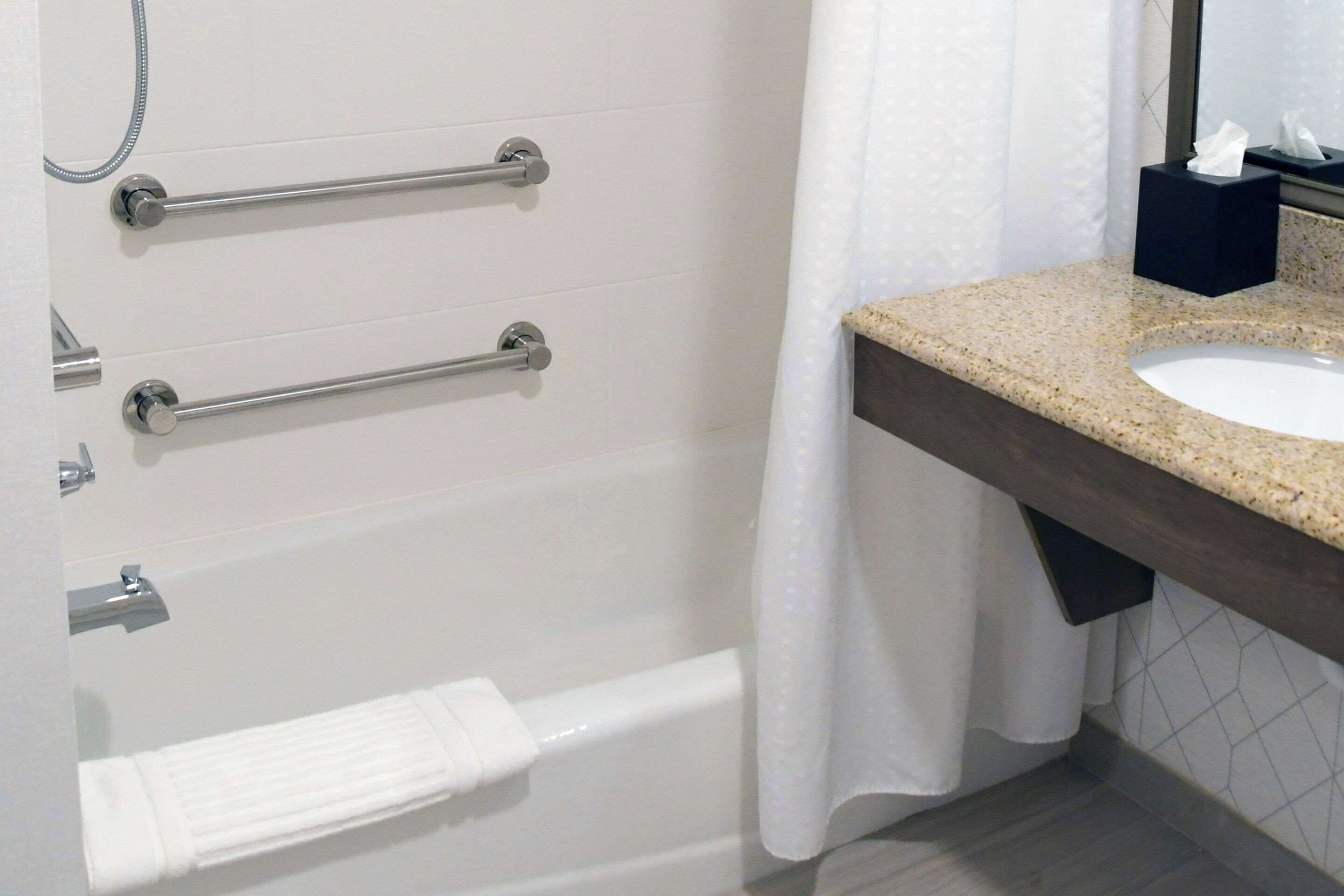 Ein Badezimmer mit einer weißen Badewanne, zwei Handtuchhaltern, einem Waschbecken mit Granitplatte und einem weißen Duschvorhang.
