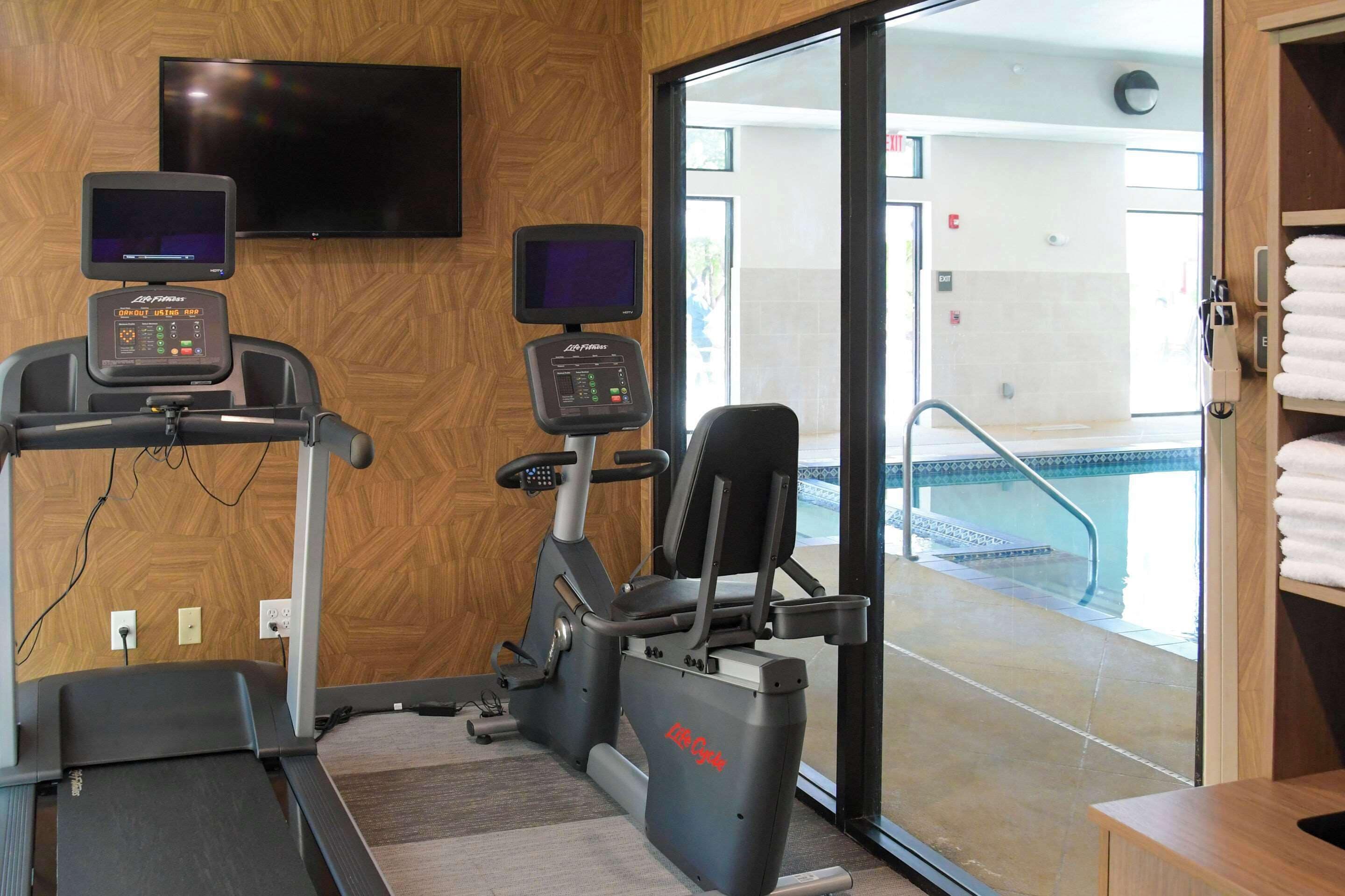 A gym with treadmills, stationary bikes, and a TV screen.