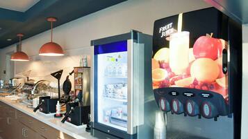 Una estación de bebidas autoservicio con múltiples dispensadores, un refrigerador y una zona de preparación de alimentos con una máquina para gofres.