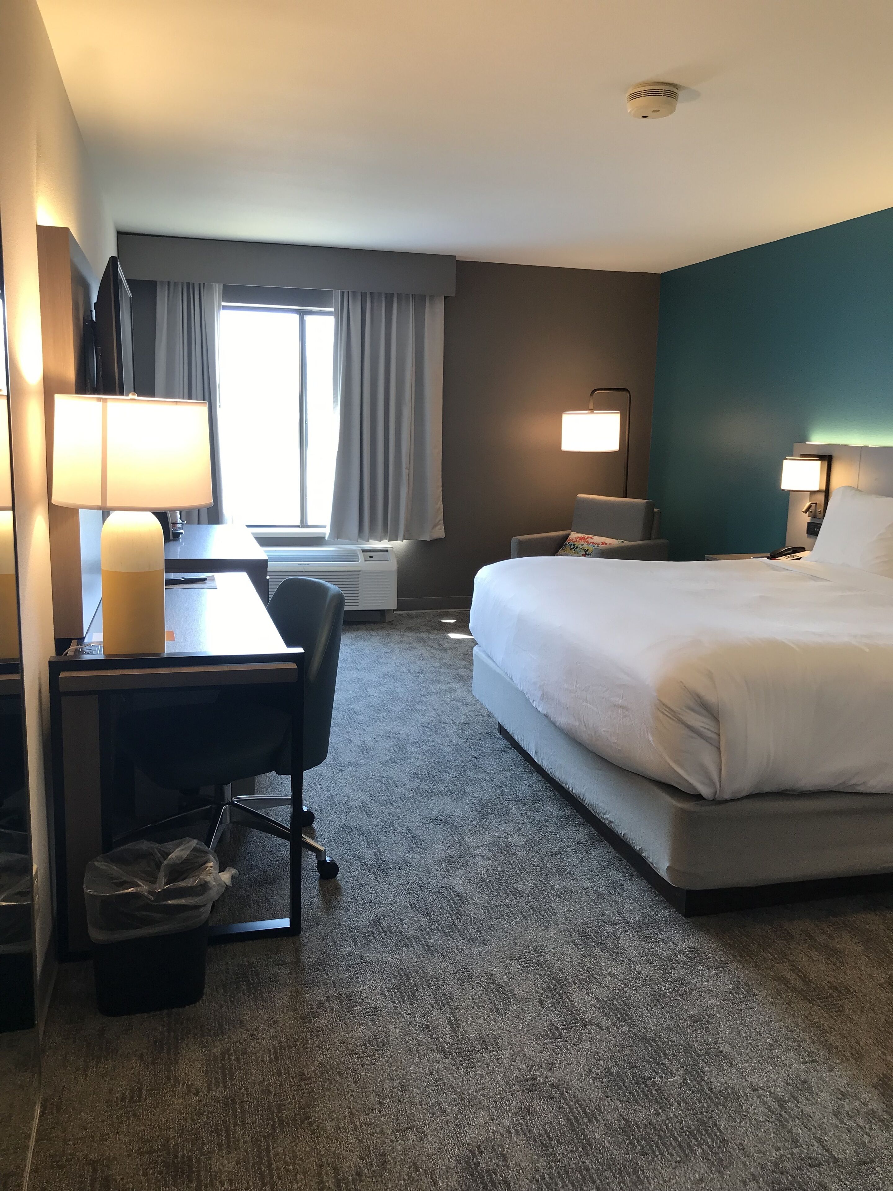 A hotel room with a bed, desk, chair, and two bedside lamps.