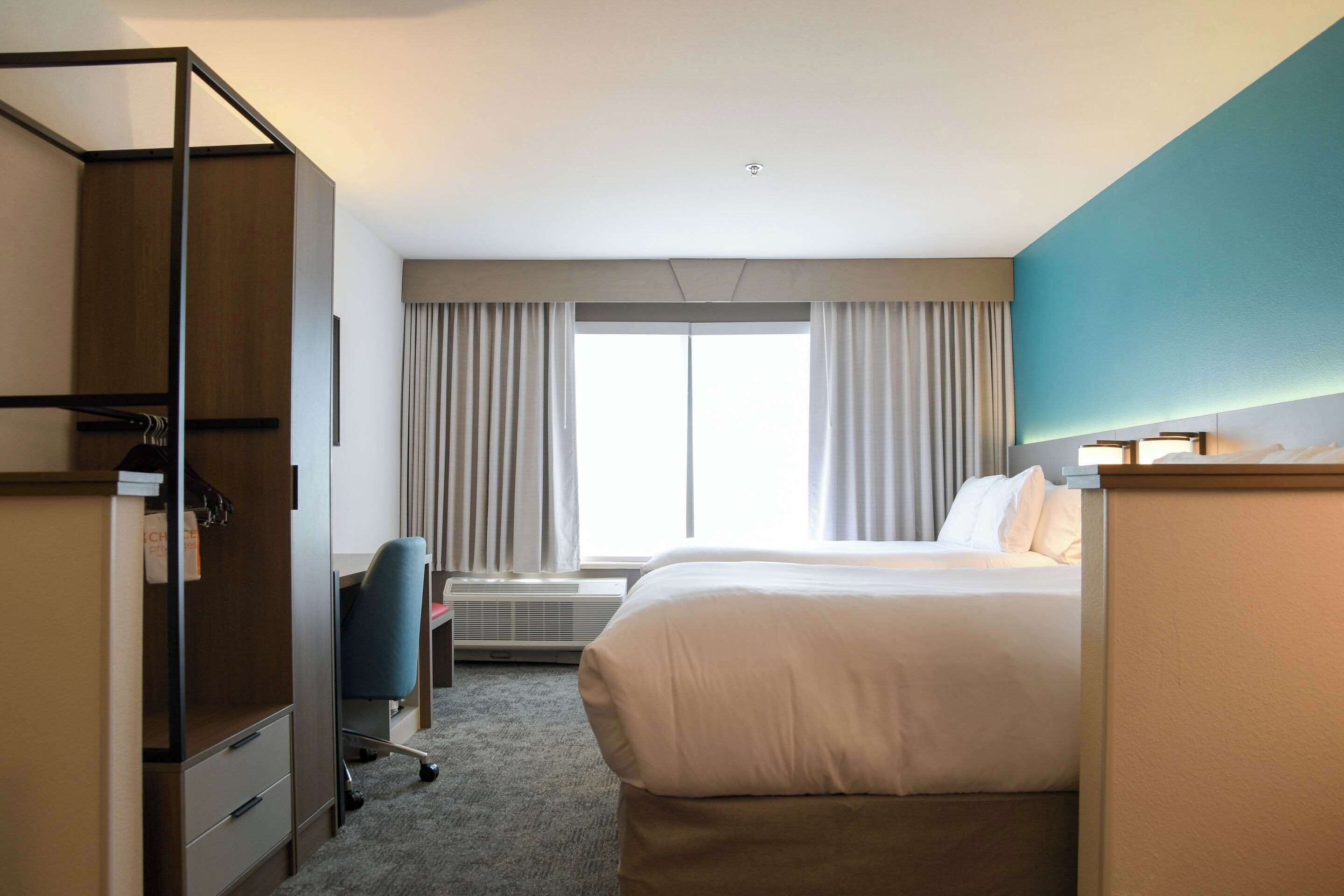 Een hotelkamer met een bed, een bureau, een stoel, een kledingkast en een groot raam met gordijnen.