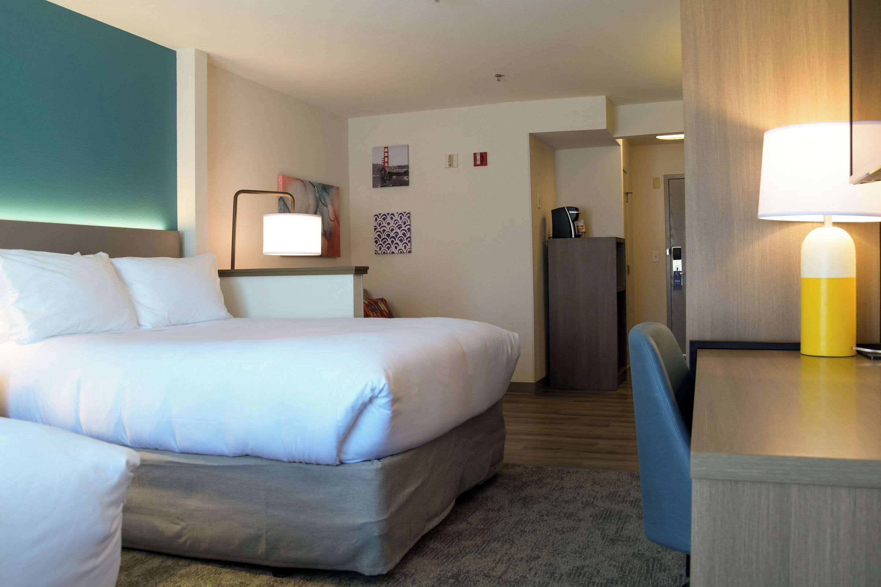 Une chambre d’hôtel avec un lit, un bureau doté d’une lampe, une chaise et une petite table.