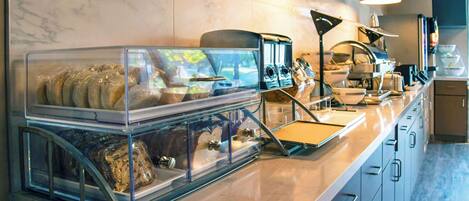Een buffetgedeelte met glazen containers gevuld met verschillende soorten eten, een koffieapparaat en een waterdispenser.