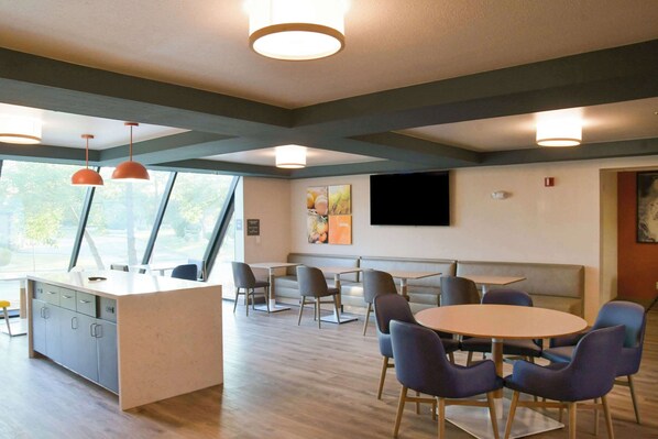 A modern hotel room with a wooden floor, a central island with a sink, a seating area with a round table and chairs, and large windows providing natural light. - Comfort Inn & Suites NW Milwaukee (Village of Germantown)