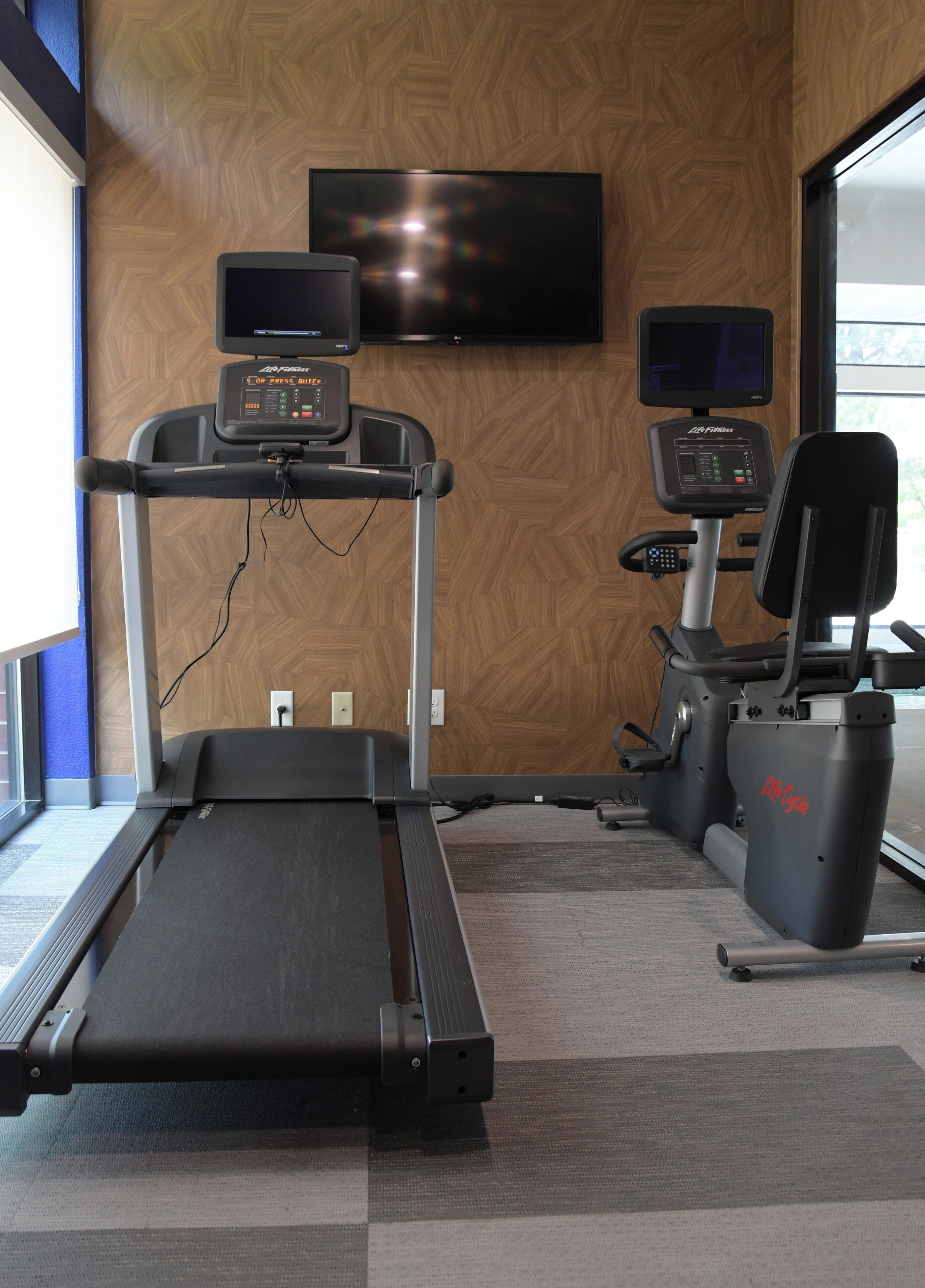 Un gimnasio con cinta de correr, máquinas de pesas y un televisor montado en la pared.