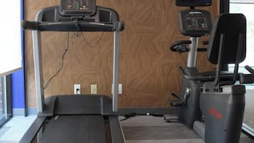 Un gimnasio con cinta de correr, máquinas de pesas y un televisor montado en la pared.
