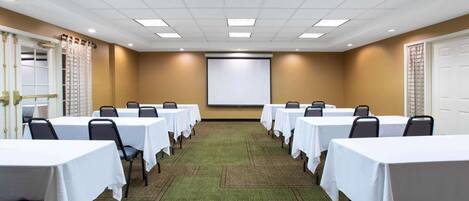 A conference room with tables and chairs, a projector screen, and a carpeted floor.