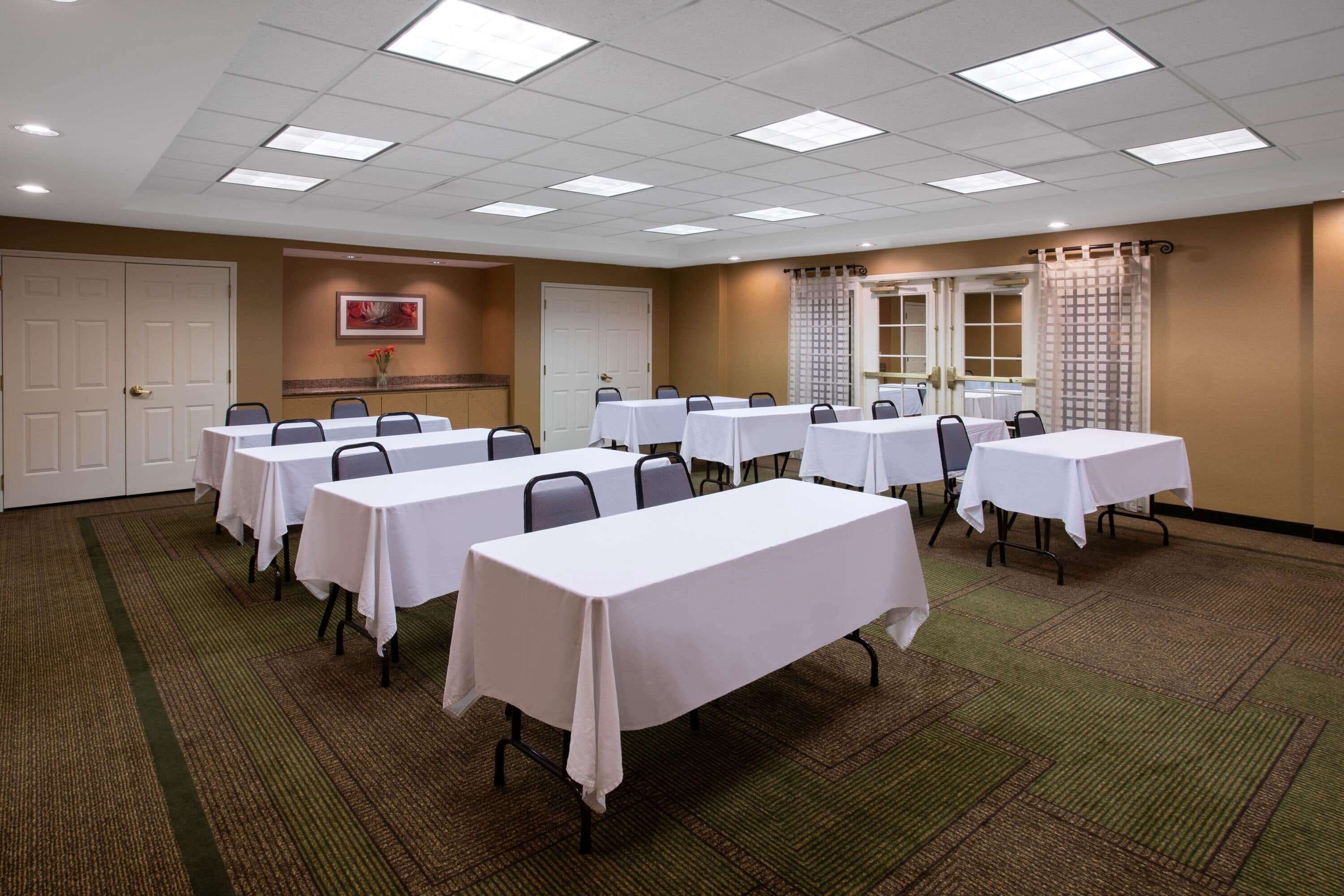 Una sala conferenze con diversi tavoli e sedie, pavimento in moquette e soffitto con faretti.