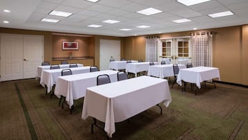 Una sala conferenze con diversi tavoli e sedie, pavimento in moquette e soffitto con faretti.
