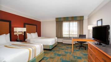 A hotel room with two beds, a desk, a television, and a window with curtains.