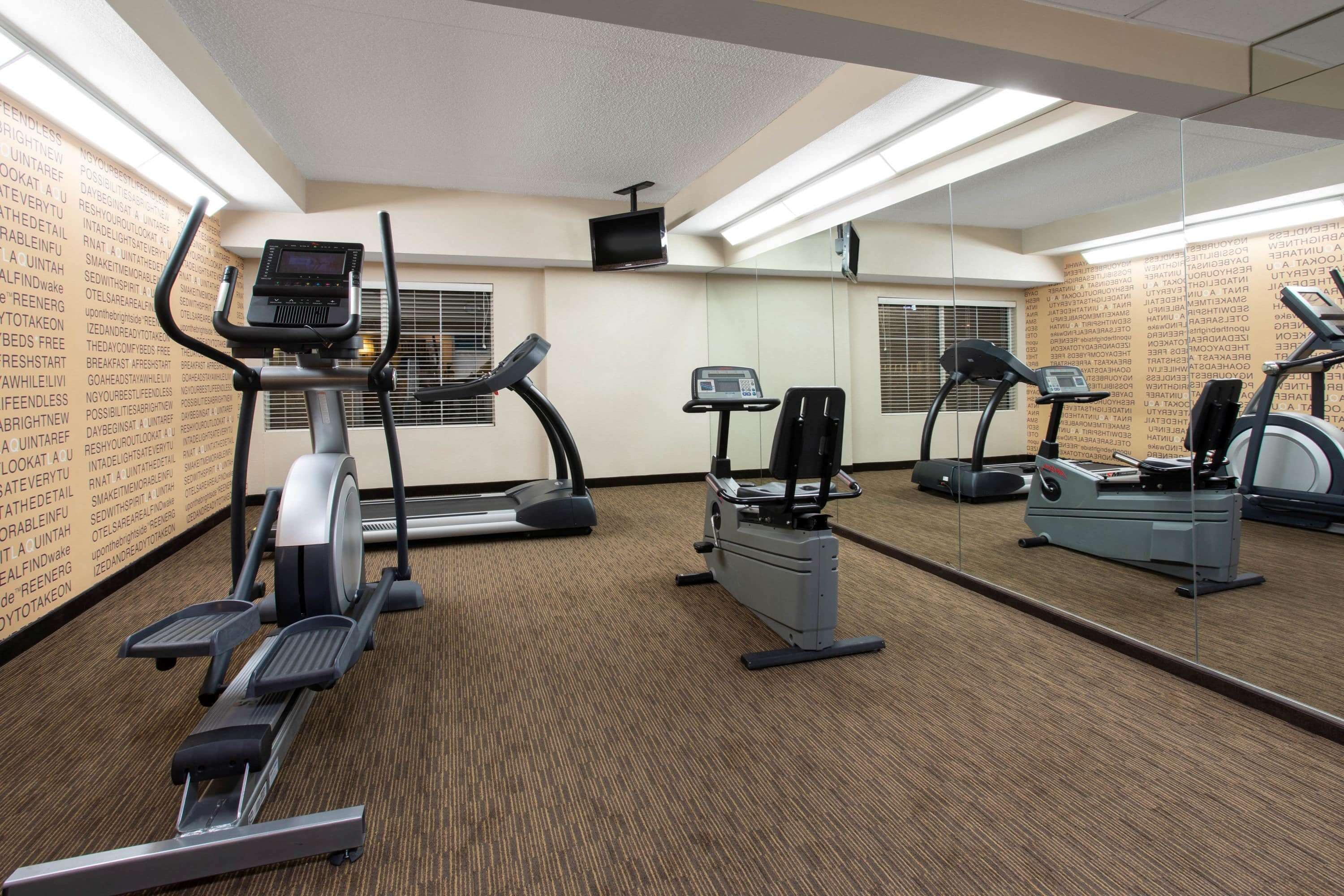 Une salle de sport équipée de tapis de course, de vélos elliptiques et d’un mur recouvert de miroirs.