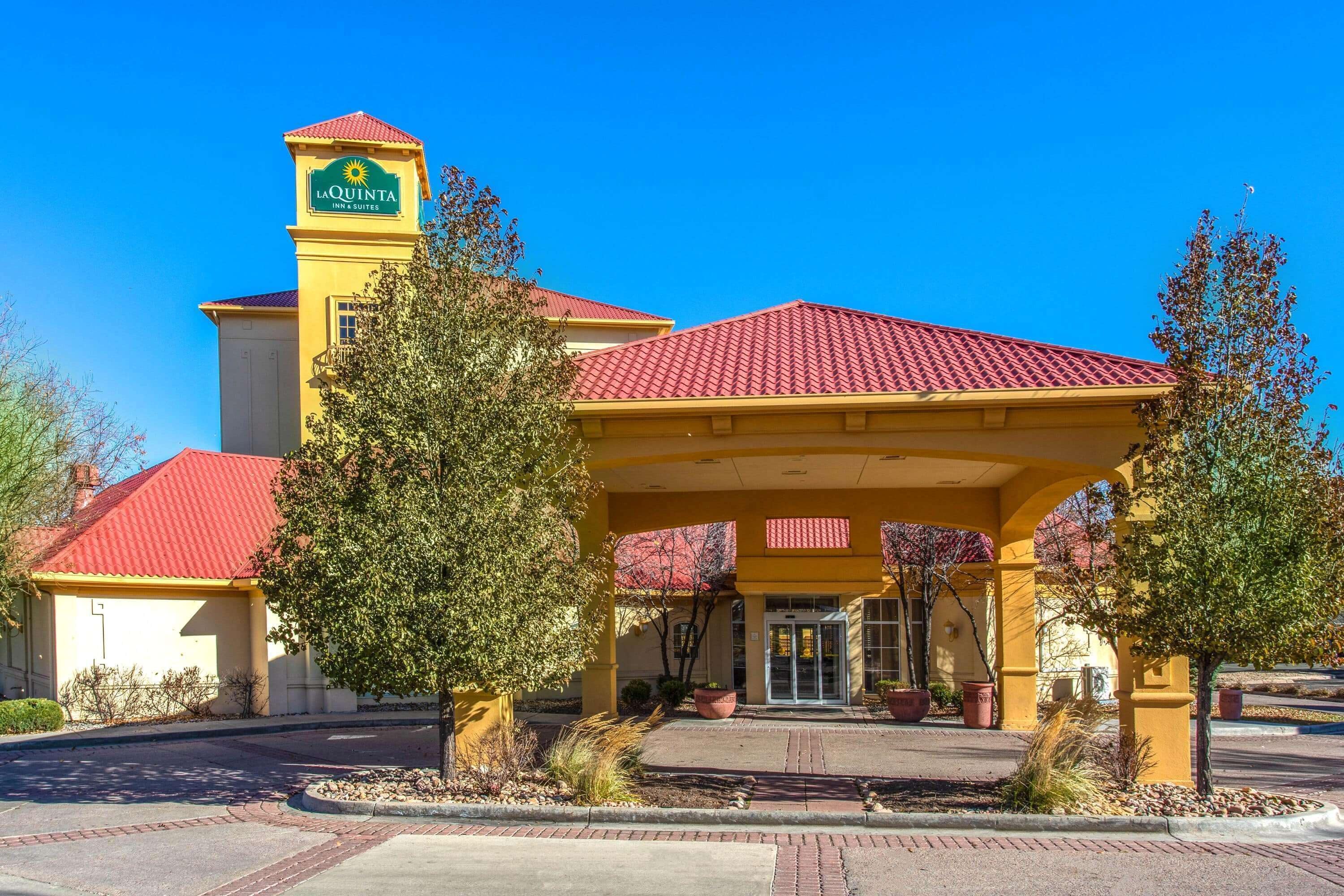 Entrada d'un hotel amb teulada vermella, façana groga i un rètol que diu "La Quinta Inn & Suites".