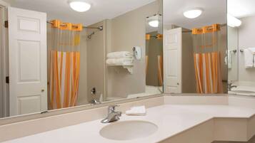 A bathroom with a large mirror, a sink, and a shower with orange curtains.