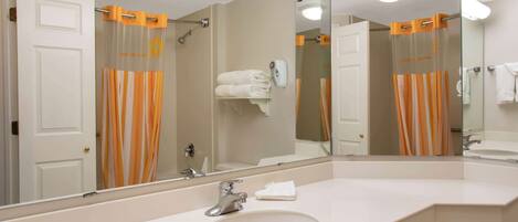 A bathroom with a large mirror, a sink, and a shower with orange curtains.