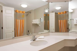 A bathroom with a large mirror, a sink, and a shower with orange curtains.
