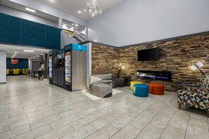 A spacious lobby with a seating area, a refreshment station, and a stone wall with a mounted TV. - Clarion Pointe Hinesville near Fort Stewart (Hinesville)