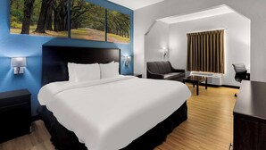 Ein Hotelzimmer mit einem großen Bett, einem Schreibtisch, einem Stuhl und einem Baumgemälde an der Wand.