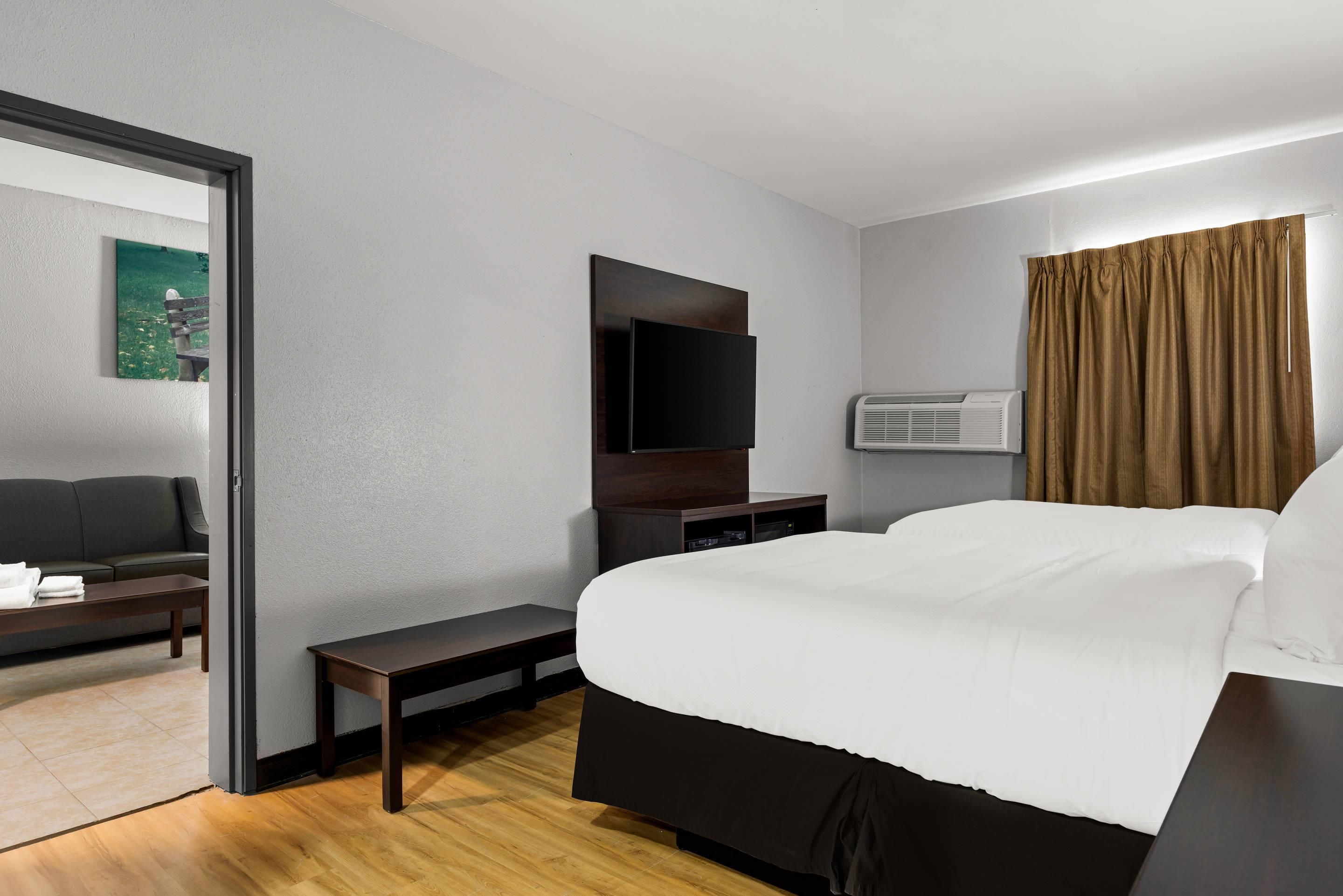 Habitación de hotel con cama, escritorio, silla, televisor de pantalla plana, aire acondicionado y ventana con cortinas.