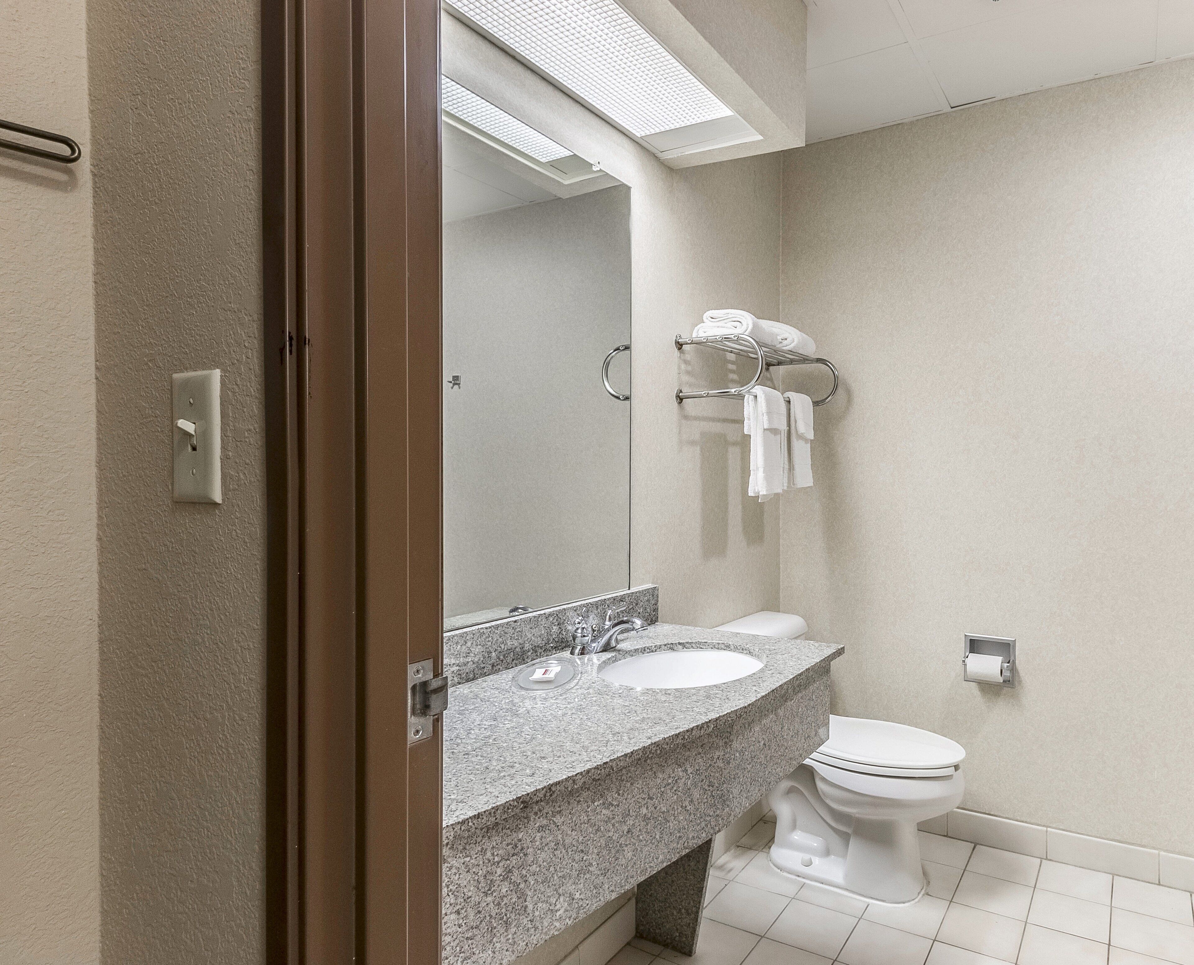 A bathroom with a granite countertop sink, a mirror, a toilet, and a towel rack with towels.
