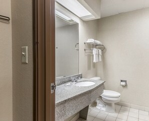 Un baño con lavamanos de encimera de granito, un espejo, inodoro y un perchero con toallas.