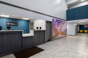 Zona de recepción de hotel con diseño moderno, que incluye un mostrador de recepción, una pantalla digital y un mural grande en la pared.