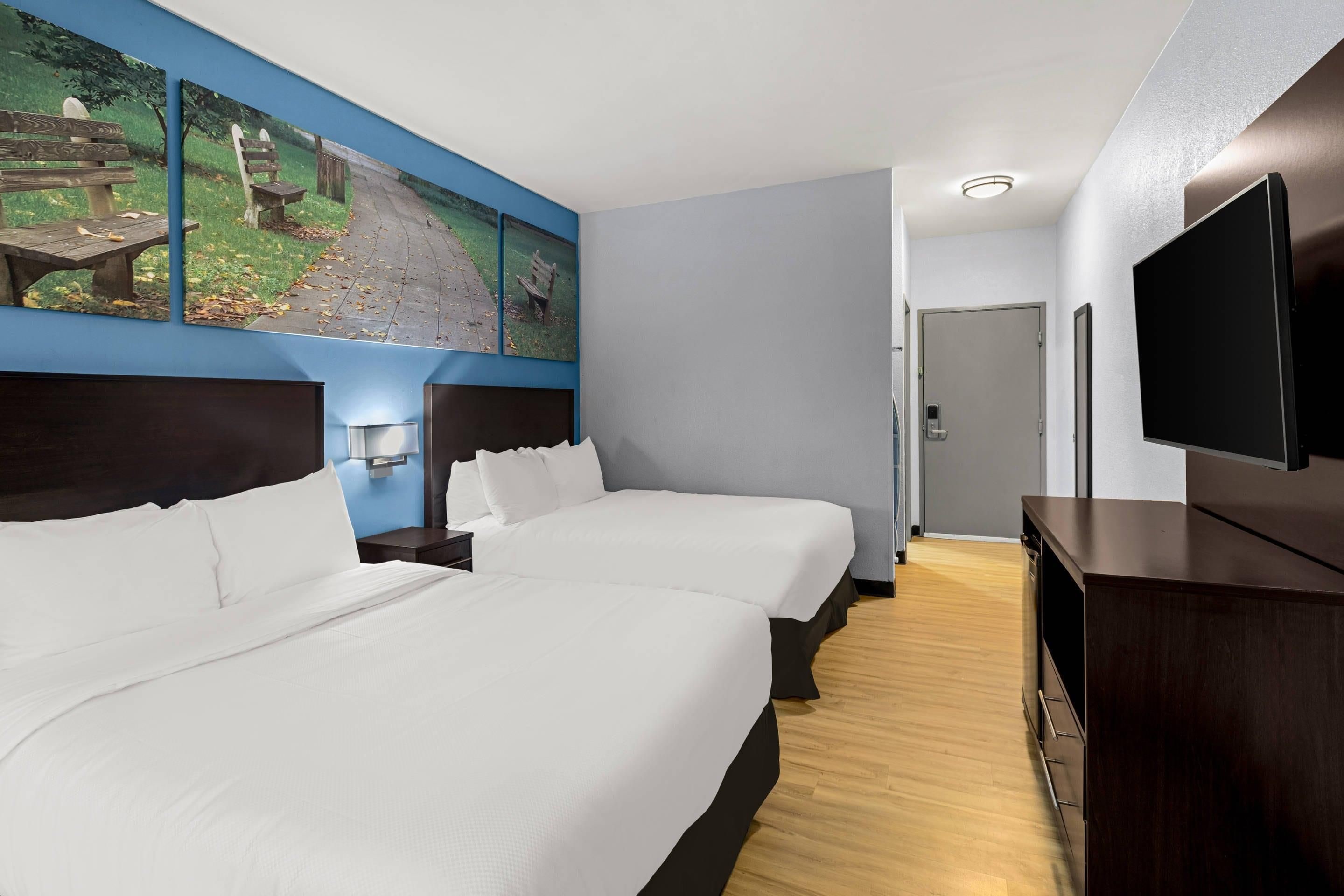 Une chambre d’hôtel avec deux lits, un téléviseur à écran plat, un tableau au mur et un plancher en bois.