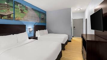 Une chambre d’hôtel avec deux lits, un téléviseur à écran plat, un tableau au mur et un plancher en bois.