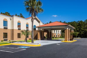 A hotel with a covered entrance, a parking lot, and a palm tree. - Clarion Pointe Hinesville near Fort Stewart (Hinesville)