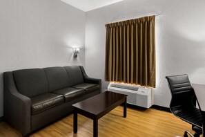 Una sala de estar moderna con un sofá de cuero, una mesa de centro de madera, una silla negra y una ventana con cortinas.