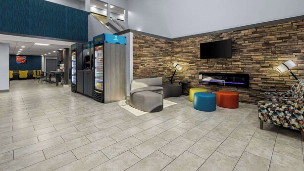 Eine geräumige Lobby mit modernem Design, inklusive einer Sitzecke mit Sofas und Poufs, einer Treppe und einem an der Wand befestigten Fernseher.