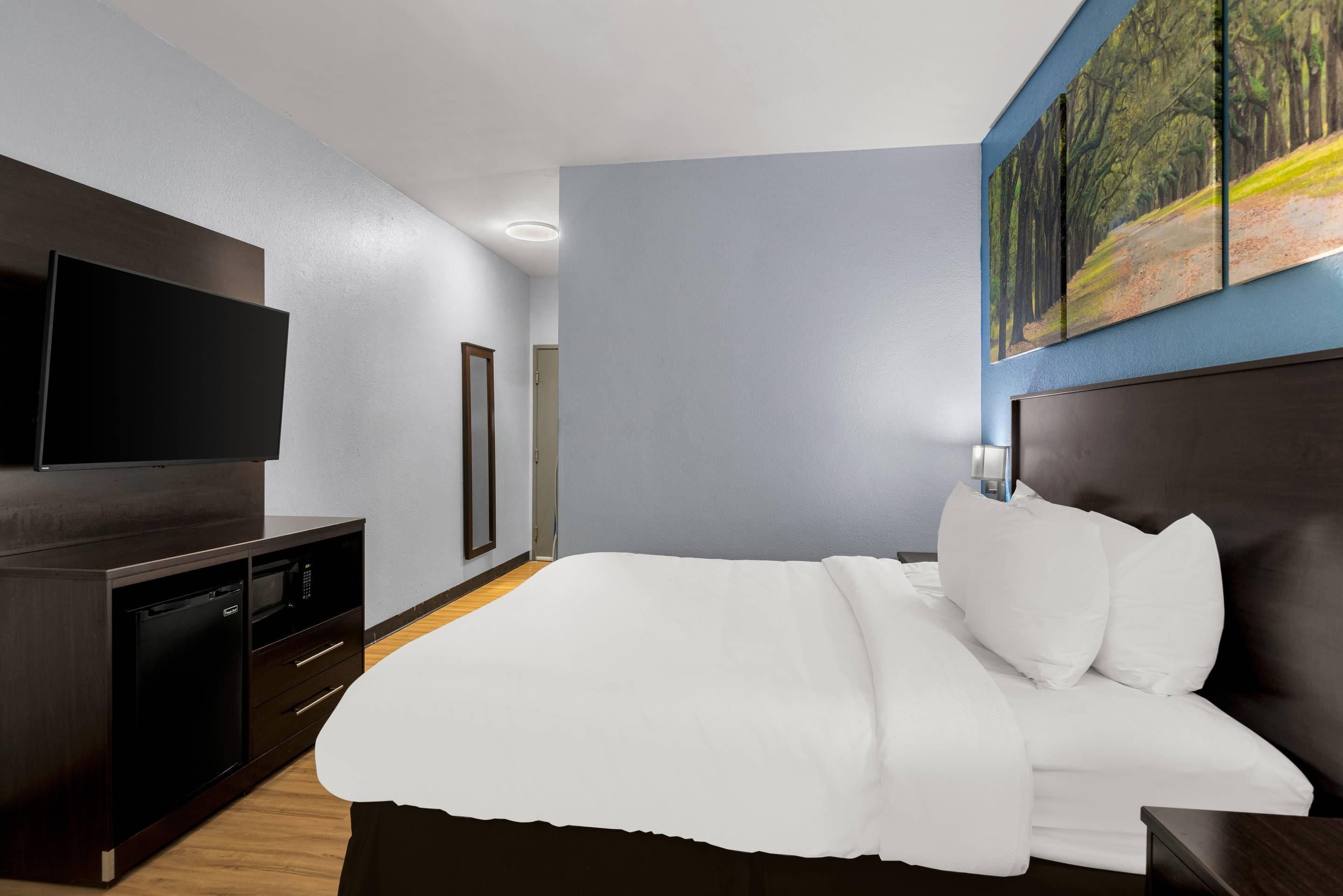 A hotel room with a large bed, a flat-screen TV, a dark wood dresser, and a painting on the wall.