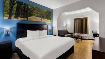 Een hotelkamer met een groot bed, een bureau, een stoel, een bureaulamp, een telefoon aan de muur en een schilderij van een bos.