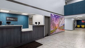 Ein Hotel-Empfangsbereich mit blauer Wandtextur, einer Rezeption, einem digitalen Bildschirm und einem farbenfrohen Wandgemälde.