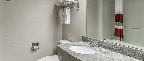 Un baño moderno con encimera de granito, inodoro blanco y cabina de ducha de vidrio.