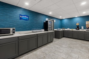 Un área de cocina moderna con una pared azul con textura, un microondas, un refrigerador y un lavamanos.